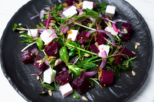 Salad of microgreen, beetroot and cheese with fresh onions and seeds on a plate.