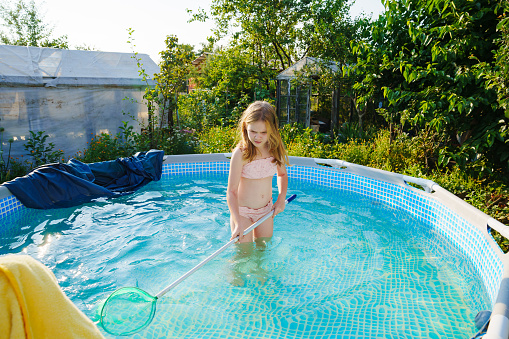 Cute teenage girl in pink swimsuit playing in a small pool. Swimming pool for the garden or yard in a country house.