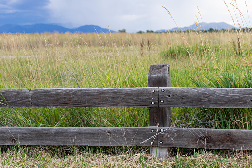 Wooden fence in a grassy field with storm approaching from the mountains