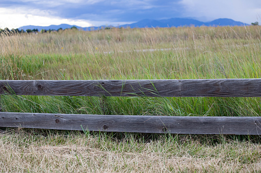 Wooden fence in a grassy field with storm approaching from the mountains