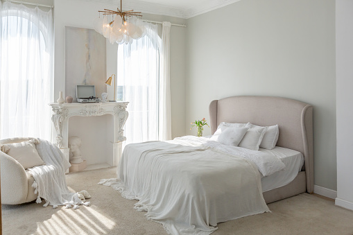a gentle cozy bright apartment with huge panoramic windows with sunlight. bedroom in soft beige tones with a fireplace and a comfortable stylish upholstered armchair and bed