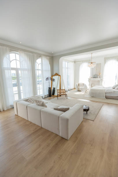 istock cozy bright apartment with huge panoramic windows with sunlight. bedroom in white and beige tones with fireplace and soft armchair. stylish living room with log coffee table and large white sofa 1646358344