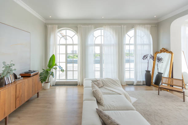 istock cozy bright apartment with huge panoramic windows with sunlight. bedroom in white and beige tones with fireplace and soft armchair. stylish living room with log coffee table and large white sofa 1646358353