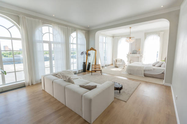 istock cozy bright apartment with huge panoramic windows with sunlight. bedroom in white and beige tones with fireplace and soft armchair. stylish living room with log coffee table and large white sofa 1646358355