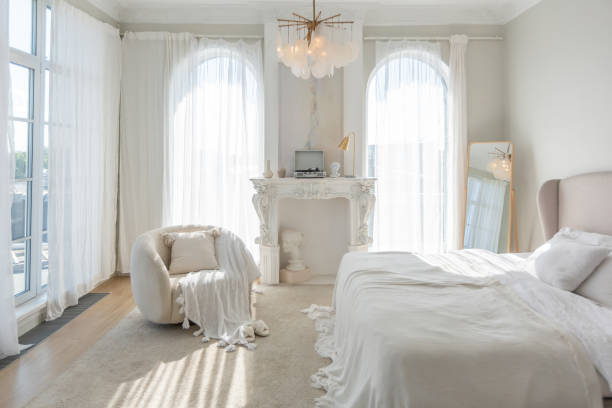 istock cozy bright apartment with huge panoramic windows with sunlight. bedroom in white and beige tones with fireplace and soft armchair. stylish living room with log coffee table and large white sofa 1646358905