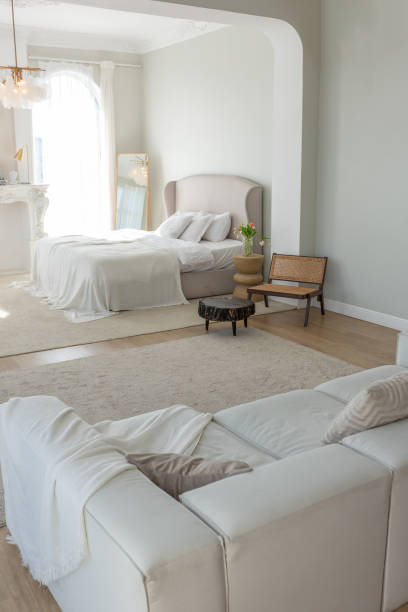 istock cozy bright apartment with huge panoramic windows with sunlight. bedroom in white and beige tones with fireplace and soft armchair. stylish living room with log coffee table and large white sofa 1646358940