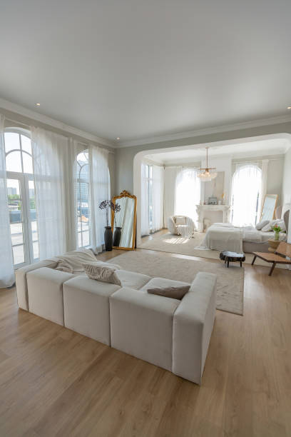 istock cozy bright apartment with huge panoramic windows with sunlight. bedroom in white and beige tones with fireplace and soft armchair. stylish living room with log coffee table and large white sofa 1646360588