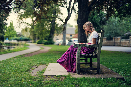 Teenage girl enjoying enjoying summer vacations in Gloucestershire, United Kingdom.\nThe girl is sitting on a bench in public park and reading a book.\nCanon R5