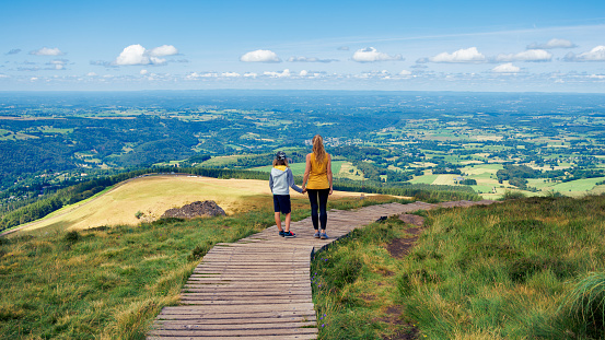 Mother and son walking on nature trail holding hands enjoying panoramic view of Auvergne landscape- travel destination, vacation,  family sport concept