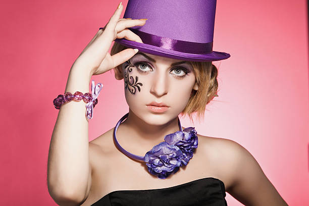 Studio photo of a beautiful teenage girl with blond hair in a violet hat on a pink background
