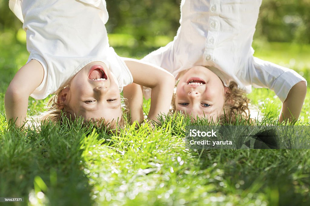 Two children doing hand stands in a garden Happy children playing head over heels on green grass in spring park Baby - Human Age Stock Photo