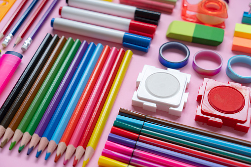 Office and school supplies arranged on pink background