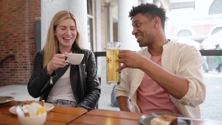 Attractive Young Adult Female And Her Black Male Friend Enjoying Their Drinks In A Cafe In London