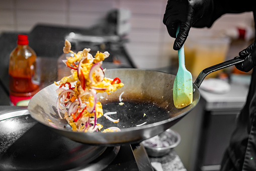 man chef cooking tasty scrambled eggs with vegetables in wok frying pan on kitchen