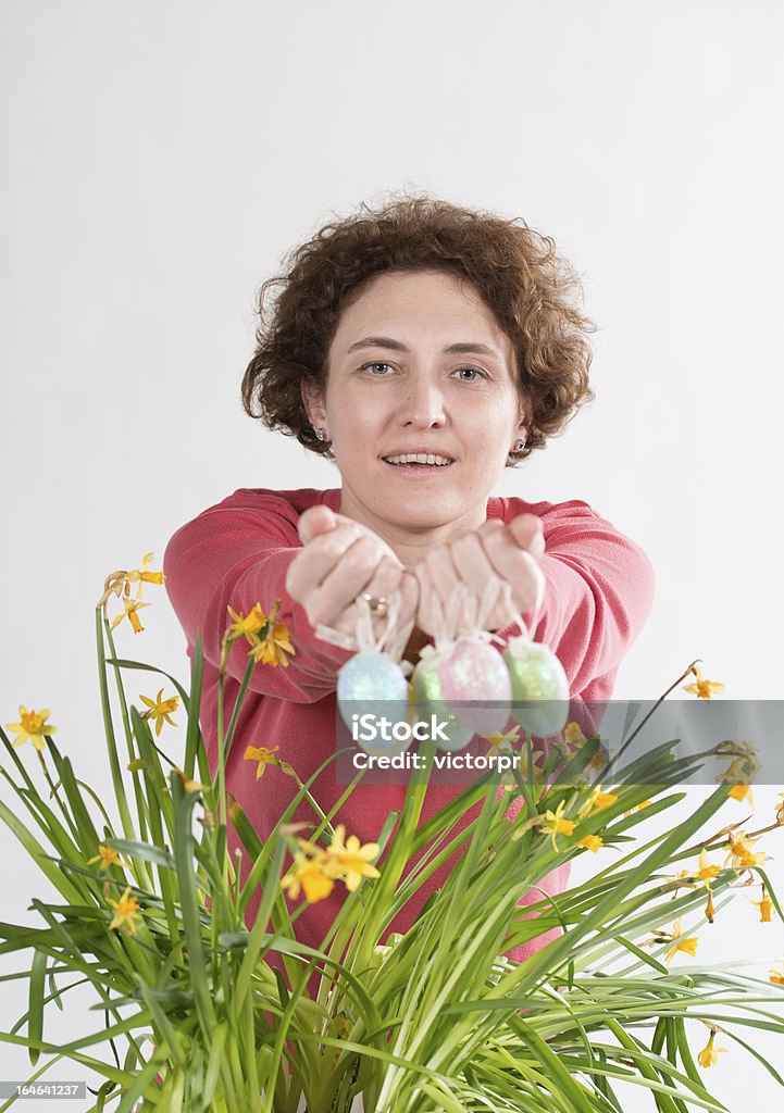 Easter eggs Young curly woman holds easter eggs and going to hide eggs in yellow narcissus Bush Stock Photo