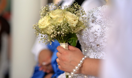 The bride is holding a beautiful wedding bouquet of white flowers. White evening dress, beautiful jewelry on the hand.
