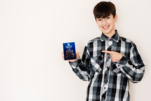 Young teenager boy holding Barbados passport looking positive and happy standing and smiling with a confident smile against white background.