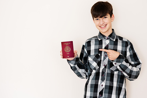 Young teenager boy holding Estonia passport looking positive and happy standing and smiling with a confident smile against white background.