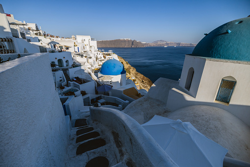 A beautiful view of the iconic blue and white houses and the sea in Santorini. The sun is partially illuminating the village. The sea is calm and blue. Beautiful and luxurious travel destinations.