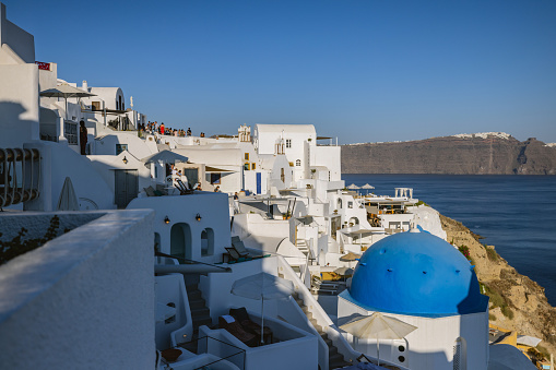 Charming village of Oia early in the morning. The sun is partially illuminating the iconic white and blue houses. The sky is blue and clear. Beautiful summer travel destination.