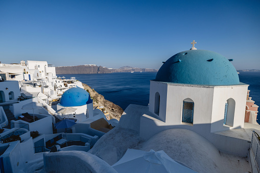 A beautiful view of the iconic blue and white houses and the sea in Santorini. The sun is partially illuminating the village. The sea is calm and blue. Beautiful and luxurious travel destinations.