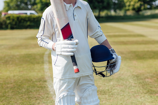 Portrait of smiling male cricket batsman wearing helmet standing on the field.