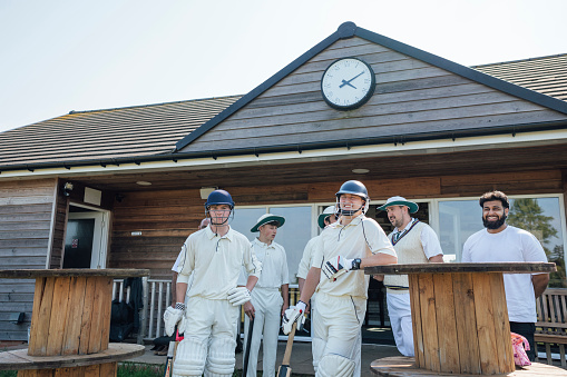 Male cricket team ready to play a game together on a sunny day in Northumberland. They are standing outside of their clubhouse wearing sports helmets.