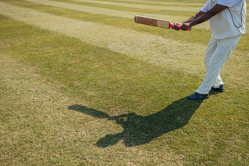 Unrecognisable male cricket player swinging a cricket bat on a pitch. It's a sunny day in Northumberland.