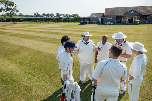 Male cricket team members ready to play cricket together. They are wearing white standing together in a huddle on a sunny day in Northumberland.