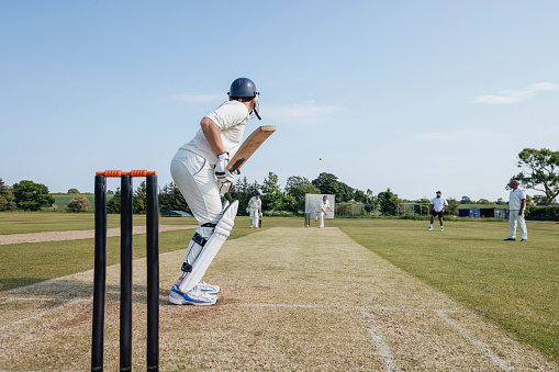 Male cricket team members playing a game together. They are wearing white enjoying the game on a sunny day in Northumberland. The men are all at their posts, batting, keeping and catching.