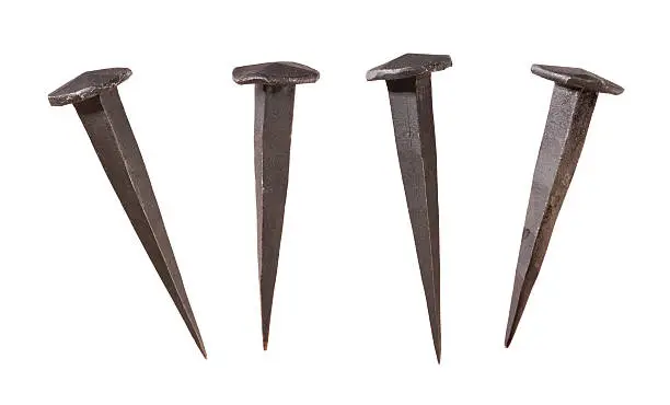 Four Antique Handmade Nails Displayed at different angles.  The metal nails are dark in color, and show a flat head coming to a sharp point at the end.  These are the kind of nails that were used by the pioneers to build log cabins. The image is isolated on a white background, and includes a clipping path.
