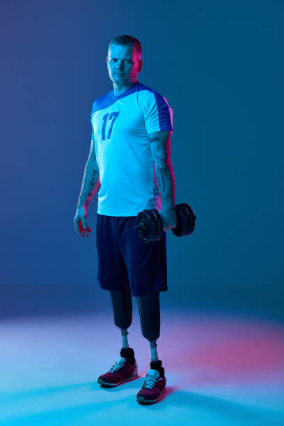 istock Confident young muscular man prosthetic legs is training with cassette dumbbells in neon light. Motivation poster. 1646464383