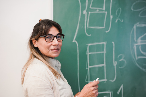 Latin female teacher smiling on camera inside classroom - Mature woman working inside university school room