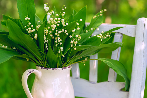 a bouquet of lilies of the valley in a ceramic vase on an old wicker sofa in a green garden. vintage style