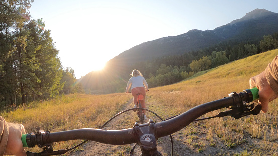 They are riding e-bikes on a double track road towards the mountains and sunrise, Crowsnest Pass,  Alberta