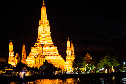 Old thai temple Wat Arun illuminated at night in Bangkok at western riverside of Chao Phraya river