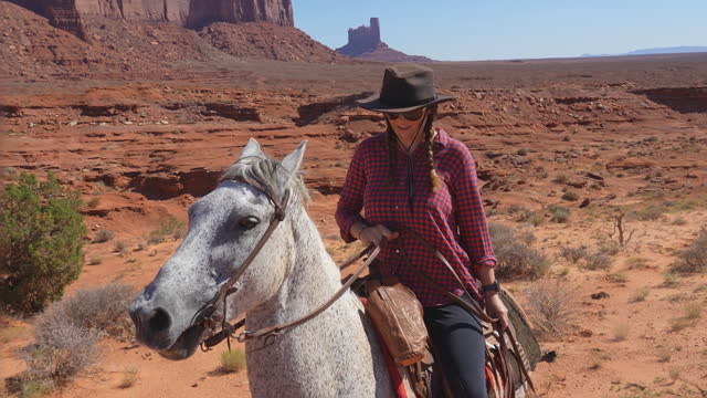 Woman riding a horse through the rocky Monument Valley in arid Arizona