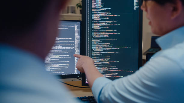 closeup group of asian people software developers using computer to write code sitting at desk with multiple screens in office at night. programmer development. - programador imagens e fotografias de stock