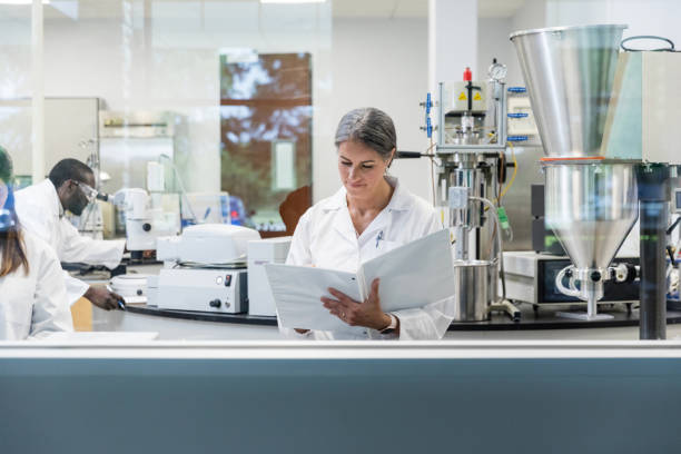 istock Female university professor updates paperwork as students work in lab 1646508449