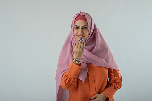 Portrait of happy woman wearing hijab and greeting adab while standing against white background