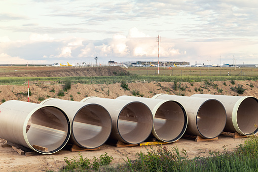 Stack of big frp composite fiberglass plastic sewage pipes at warehouse construction site near Leipzig Halle airport against blue sky background. Highway road construction infrastructure earthworks.