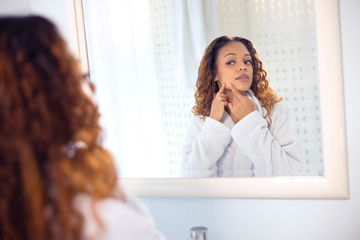 Beauty, mirror or girl checking pimples or face in morning skincare routine in bathroom at home. Facial treatment, wellness or natural woman with acne cosmetics looking at reflection for results