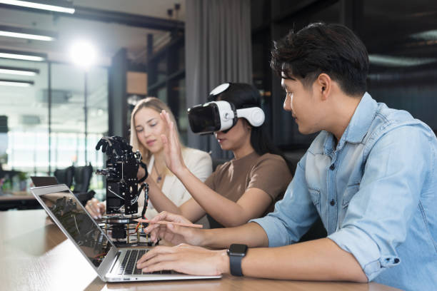 Male and female engineer working with vr glasses control AI robot arm system in workshop. Male engineer using laptop computer for training Programmable logic controller robotics arm system project ingeniero masculino y femenino que trabaja con gafas vr controlan el sistema de brazo robótico ai en el taller. ingeniero masculino usando computadora portátil para entrenamiento proyecto de sistema de brazo robótico de controlador lógico programable