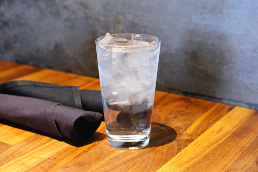 Glass of water with ice on restaurant table food and drink background texture close up photo with copy space.