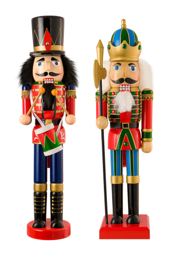 Two wooden Christmas Nutcrackers standing side by side. One  nutcracker is a drummer.  One figurine has black hair, and the other figurine has white hair.  Nutcrackers are used to crack open nuts, but can also be used as colorful Christmas decorations. The image is isolated on a white background.
