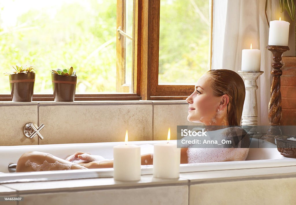 Woman taking bath Picture of beautiful woman taking bath at home, cute female lying down in bathtub, warm candle light, romantic atmosphere, pampering and hygiene, spa resort in hotel, zen balance concept Adult Stock Photo