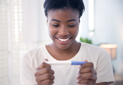 Smile, pregnancy test and black woman with positive results, happy and excited in her house. Pregnant, testing and African female person hand holding home kit with ivf or fertility treatment success