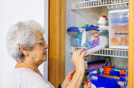 Self care routine for senior woman. Retired woman arranging pillboxes in medicine cabinet at home. Time before grandchildren visit