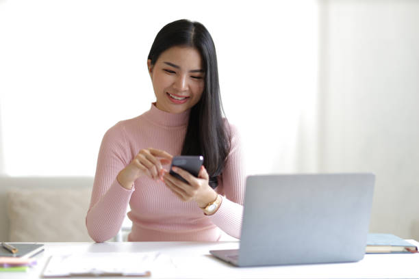 istock Attractive young Asian woman using smartphone in office at home. 1646568312