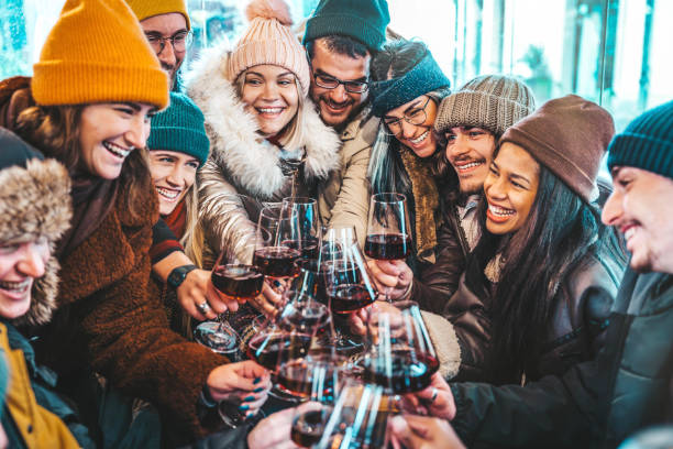 happy multiracial friends toasting red wine at restaurant terrace - group of young people wearing winter clothes having fun at outdoors winebar table - dining life style and friendship concept - apres ski fotos imagens e fotografias de stock